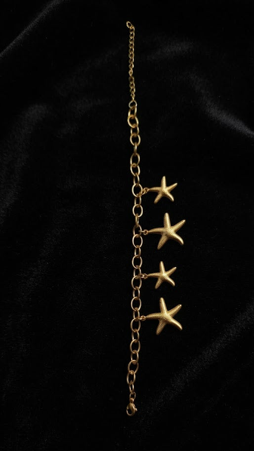 Gold starfish dangle charm bracelet on black velvet background showing four sea star charms – AureliaBlends