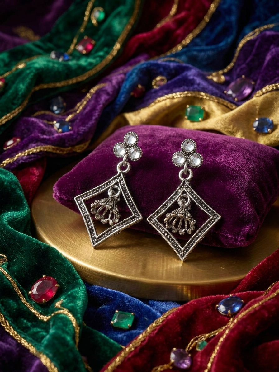 Close-up of oxidised silver pearl trefoil stud and open diamond frame with miniature jhumka bell pendant on black satin with black and silver pearls – AureliaBlends statement earrings