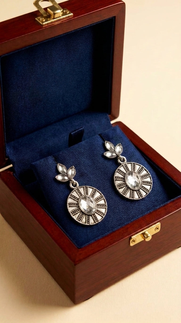 Oxidised silver marquise leaf and engraved disc drop earrings with clear crystal stones flat lay on cream satin with white rose, eucalyptus, gold leaf and scattered pearls – AureliaBlends