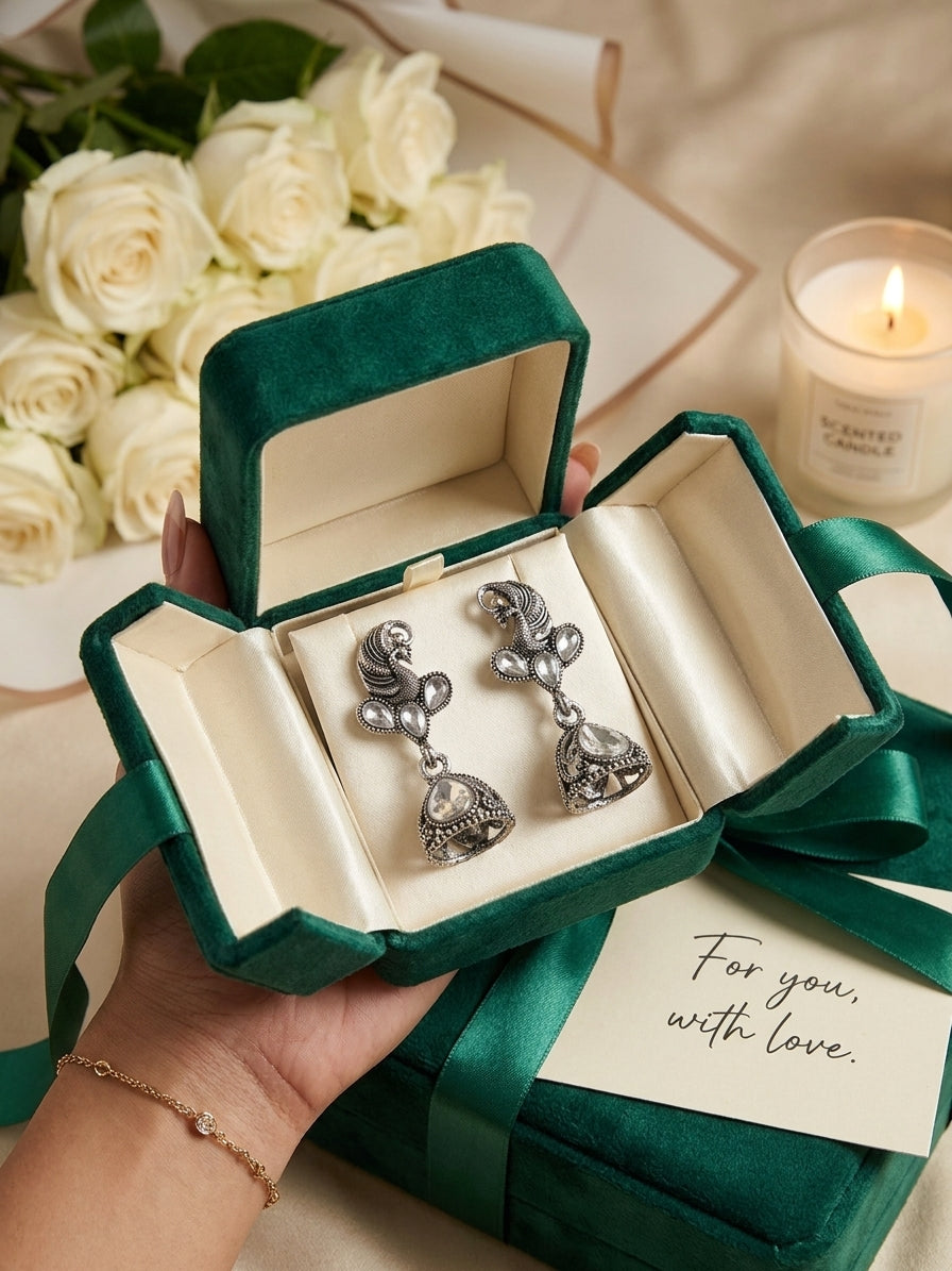 Oxidised silver peacock CZ kundan and jhumka bell drop earrings in open forest green velvet gift box with cream satin lining and For You With Love card on jewel-toned silk with ranunculus, orchids, gold frame and scattered gemstones – AureliaBlends festive ethnic earrings
