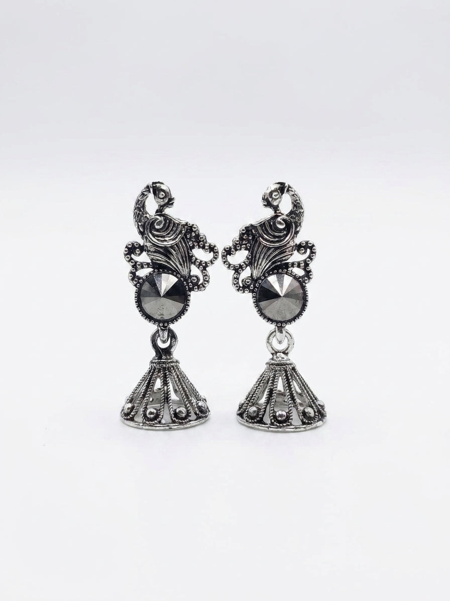 Oxidised silver peacock scroll filigree and hematite rivoli jhumka bell drop earrings flat lay on white marble with scattered black pearls, dried cream buds, antique silver trinket box and blue silk saree – AureliaBlends ethnic earrings