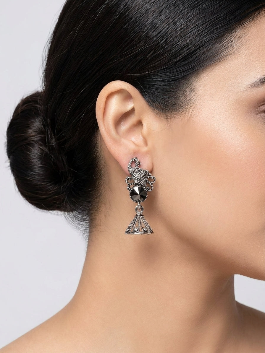 Oxidised silver peacock scroll and hematite rivoli jhumka bell drop earrings flat lay on jewel-toned green blue and red brocade velvet fabric with scattered amethyst garnet and amber gemstone cabochons – AureliaBlends festive ethnic earrings