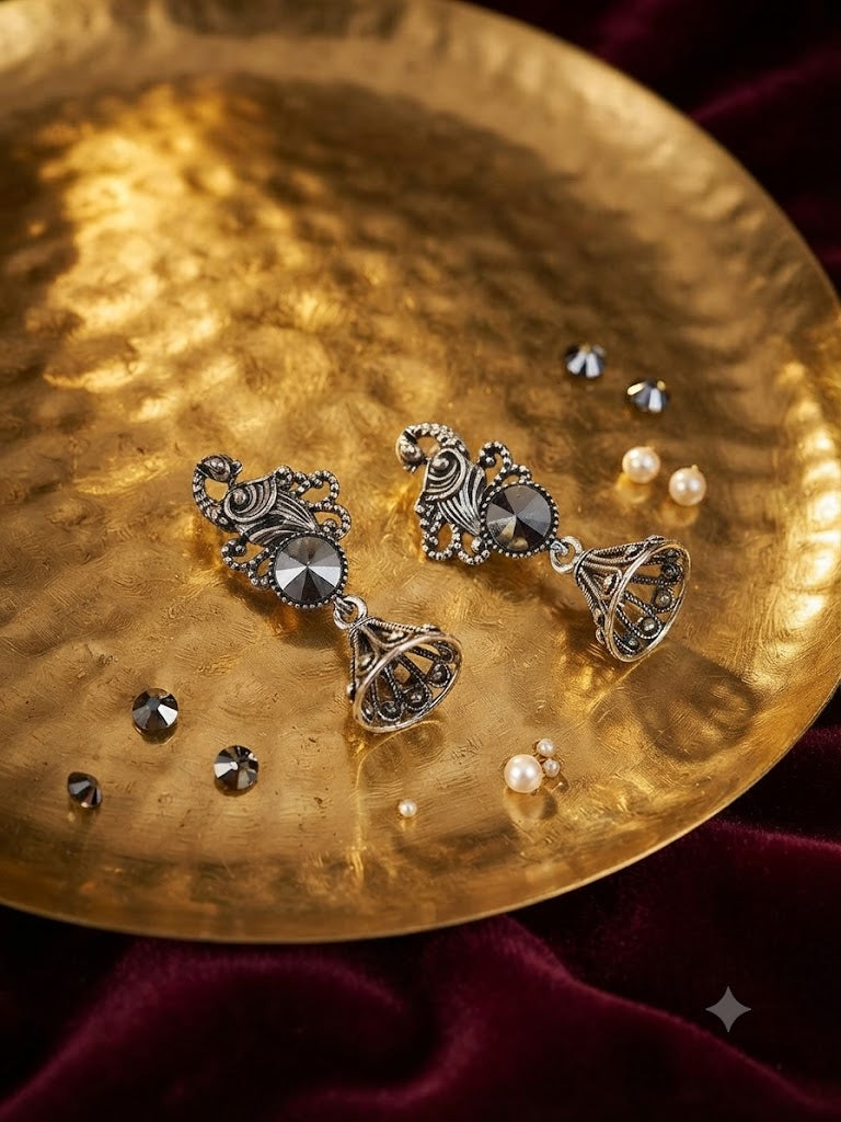 Close-up detail of oxidised silver peacock scroll filigree stud with large faceted hematite gunmetal rivoli crystal and conical open-rib jhumka bell with rope-twist ribs and beaded dots – AureliaBlends antique silver earrings