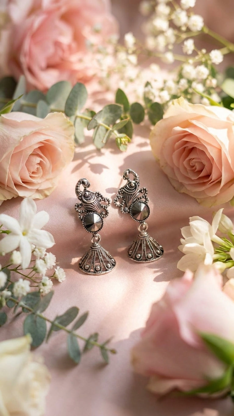 AureliaBlends oxidised silver peacock scroll hematite rivoli jhumka bell drop earrings editorial lifestyle flat lay on white marble with black pearls antique silver trinket box and blue silk saree