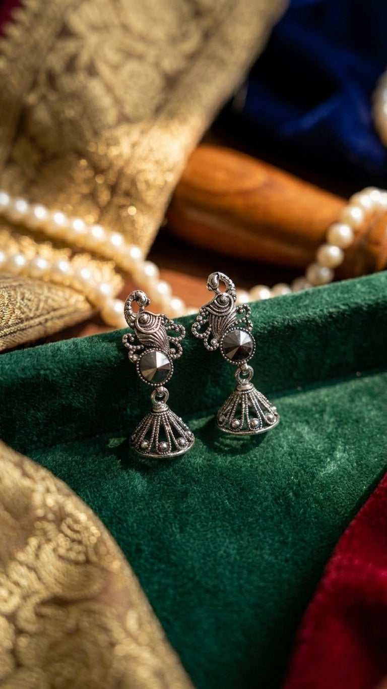 Oxidised silver peacock scroll and hematite rivoli jhumka bell drop earrings lifestyle flat lay on hammered gold thali with scattered hematite crystals pearls and dark burgundy velvet – AureliaBlends luxury ethnic earrings