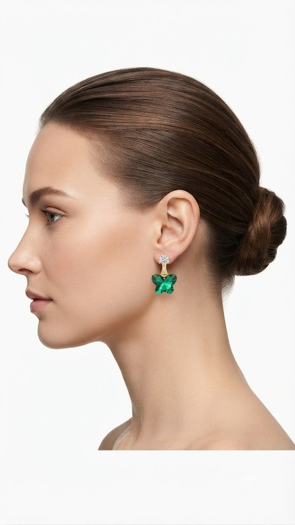 Gold-plated CZ stud and emerald green faceted butterfly crystal drop earrings editorial flat lay on cream background with scattered crystal elements – AureliaBlends butterfly crystal earrings