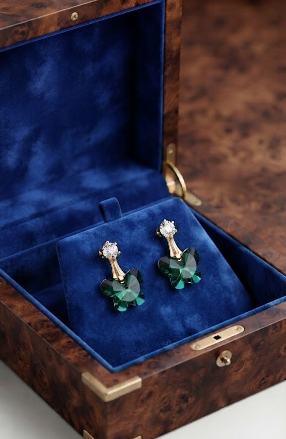 AureliaBlends gold-plated CZ stud and emerald green faceted butterfly crystal drop earrings lifestyle editorial in burl walnut wood jewellery box with royal blue velvet lining and gold brass corners
