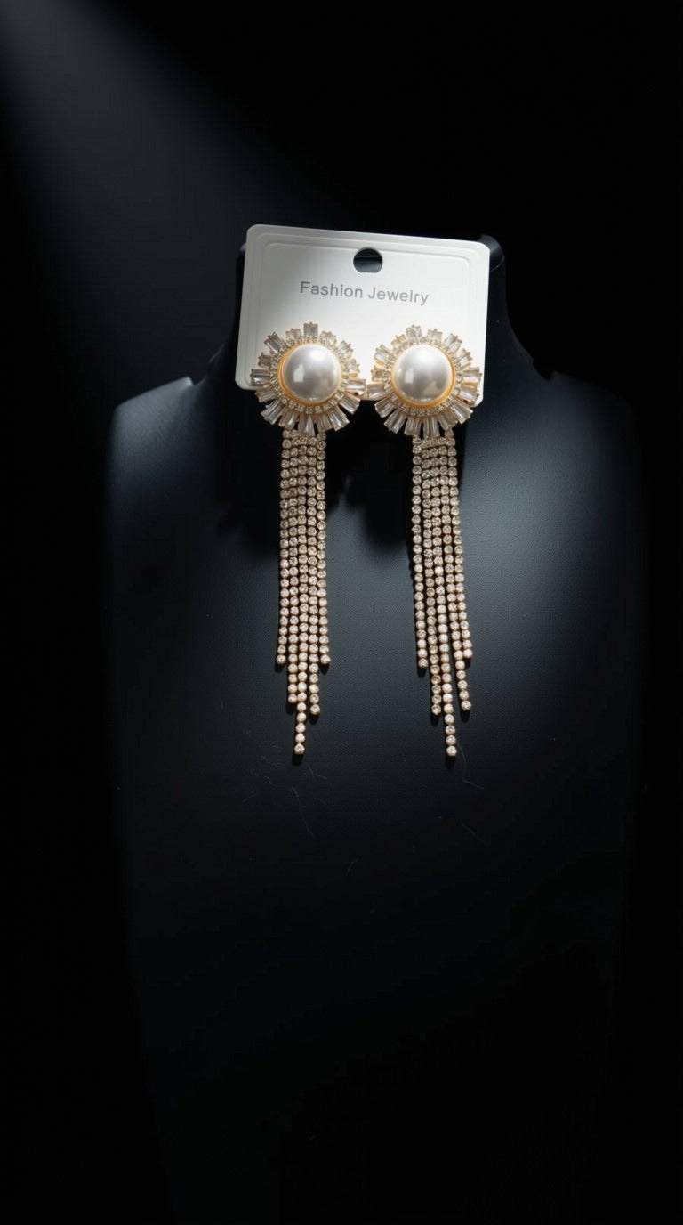 A pair of gold-toned statement dangle earrings with pearl-like round centers and multiple cascading bead chains, displayed on a black jewelry bust against a black background. A white card at the top reads 'Fashion Jewelry'.