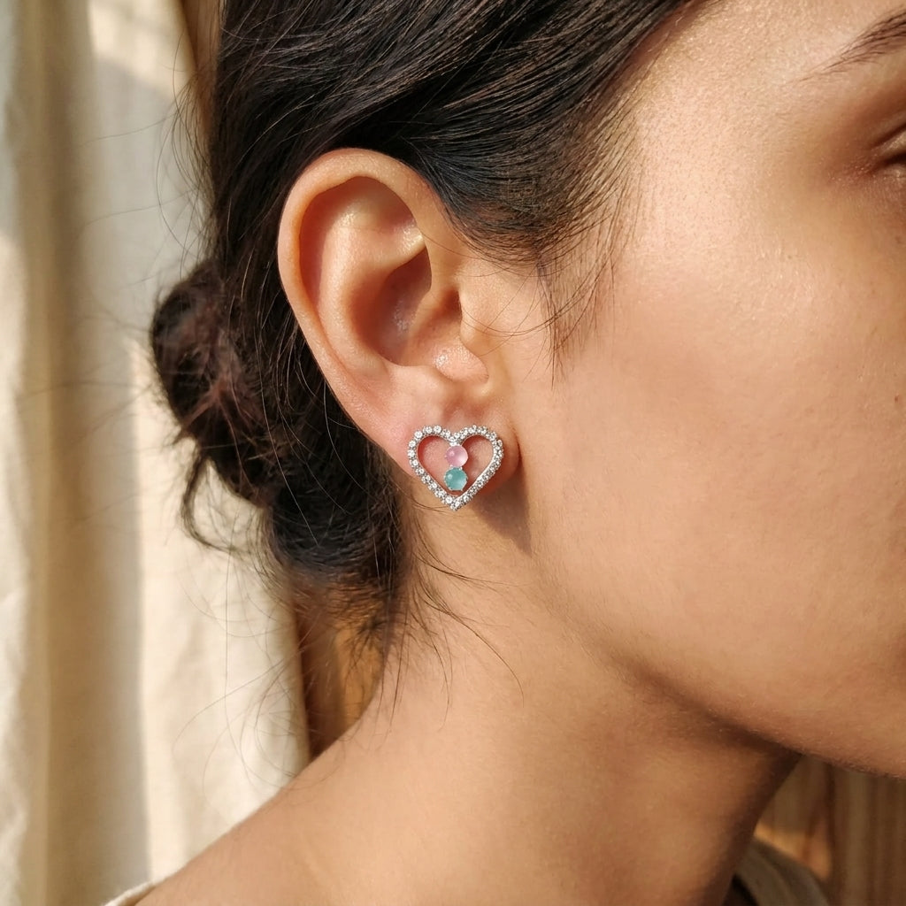 Silver pavé CZ open heart pink and aquamarine stone stud earrings flat lay on a white glitter jewellery card on champagne satin with blush roses, rose petals, baby’s breath, a vintage silver tray, white ribbon spool and a floral gift box – AureliaBlends