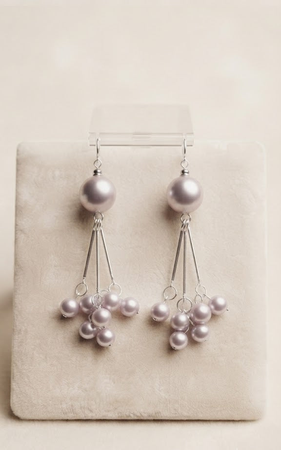 Silver lavender grey pearl cluster chandelier drop earrings hanging on a display rail against a dark black background with a burl wood panel and a four-pointed star sparkle – AureliaBlends statement dangle earrings dark editorial