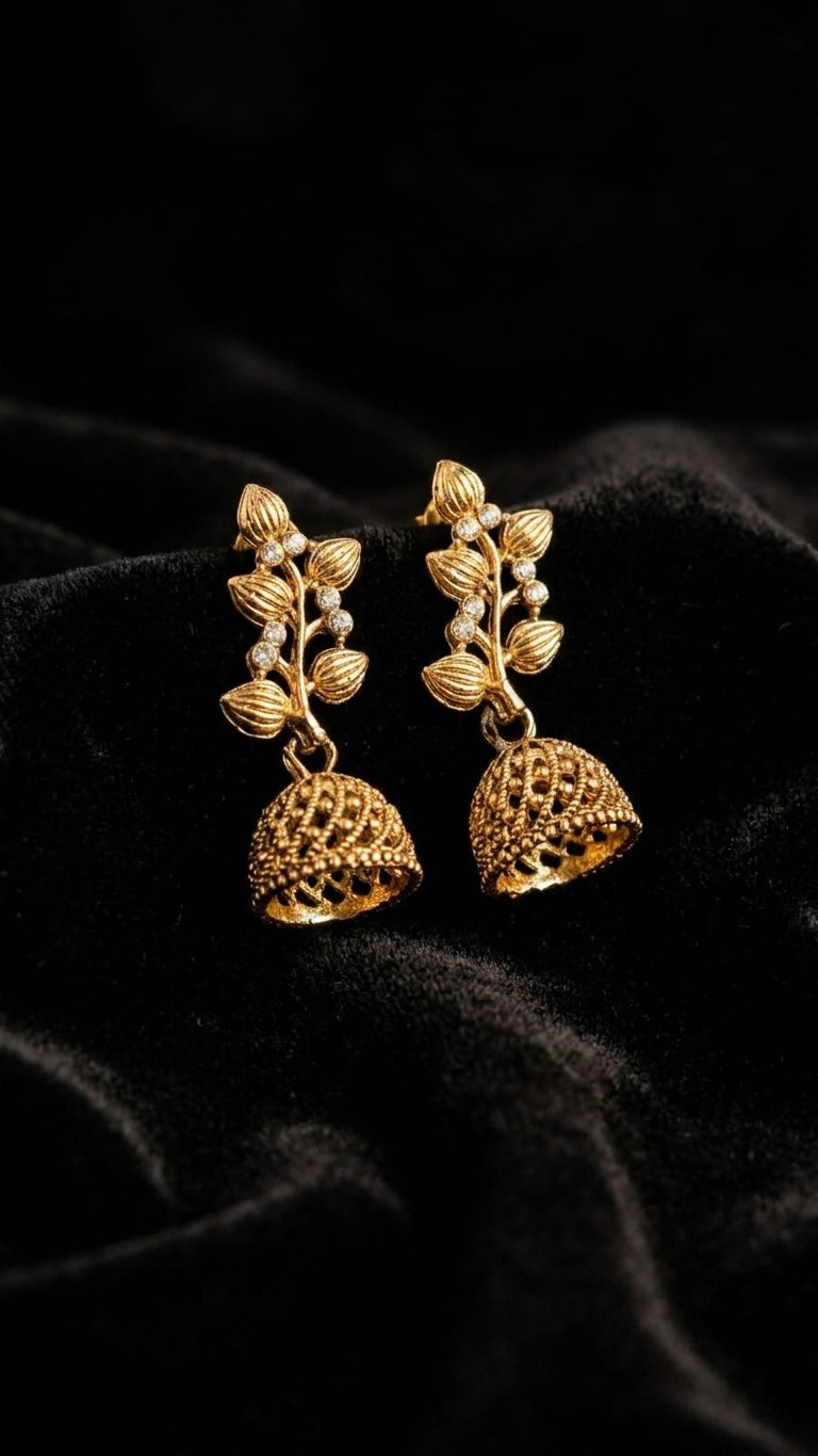 AureliaBlends gold-plated CZ botanical leaf vine and open filigree dome jhumka bell drop earrings lifestyle editorial flat lay on cream satin with antique gold hand mirrors and jasmine flowers