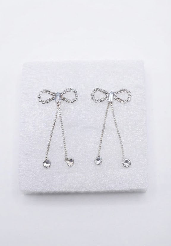Silver CZ open bow tassel chain drop earrings flat lay on grey satin with white jasmine flowers, a chain-print silk scarf, a gold fountain pen and a red jewellery box on grey background – AureliaBlends lifestyle shot