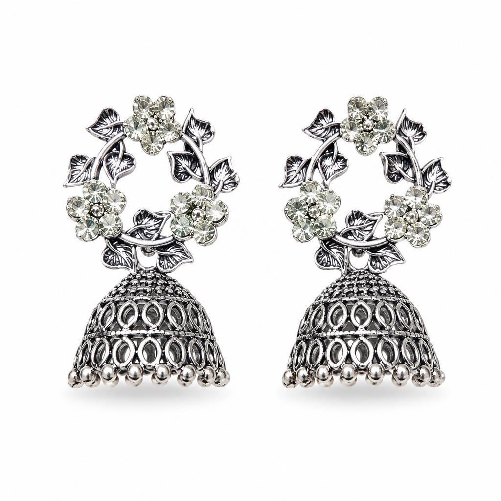 Oxidised silver CZ floral wreath and open oval lattice jhumka bell drop earrings flat lay on cream white satin with large white dahlia flower gypsophila and gold-rimmed ceramic dish – AureliaBlends ethnic jhumka earrings