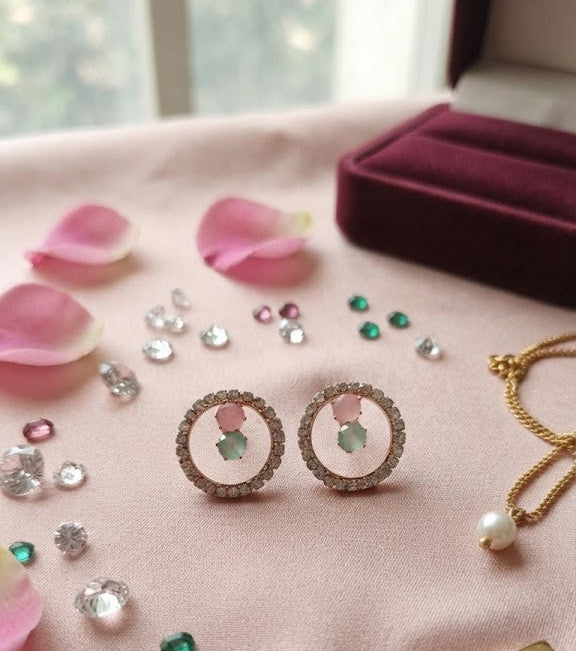 Rose gold pavé CZ open circle halo pink and mint stone stud earrings in an open navy blue velvet gift box with black velvet cushion on a dark wooden surface with scattered loose CZ stones and gold beads – AureliaBlends luxury bridal earrings