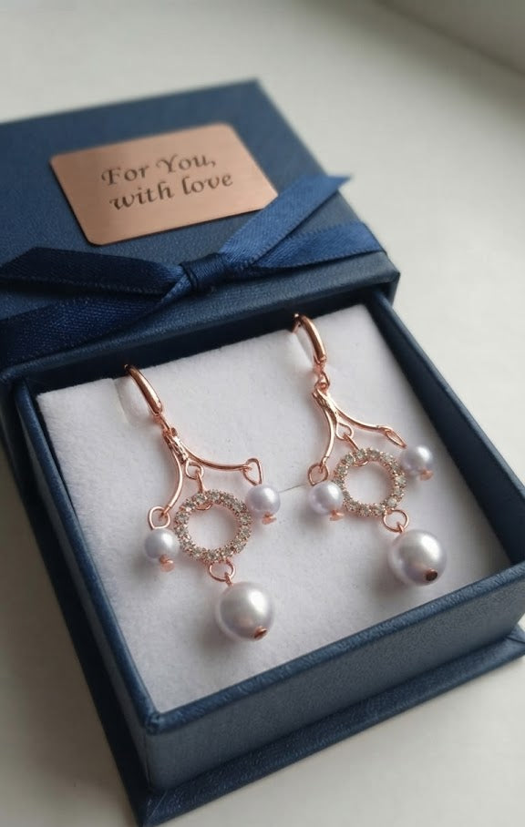 Rose gold CZ pavé circle pearl chandelier leverback drop earrings on dark black velvet with scattered gold confetti dots showing fan frame, pavé CZ circle halo, small pearl accents and large pearl drop detail – AureliaBlends dark editorial