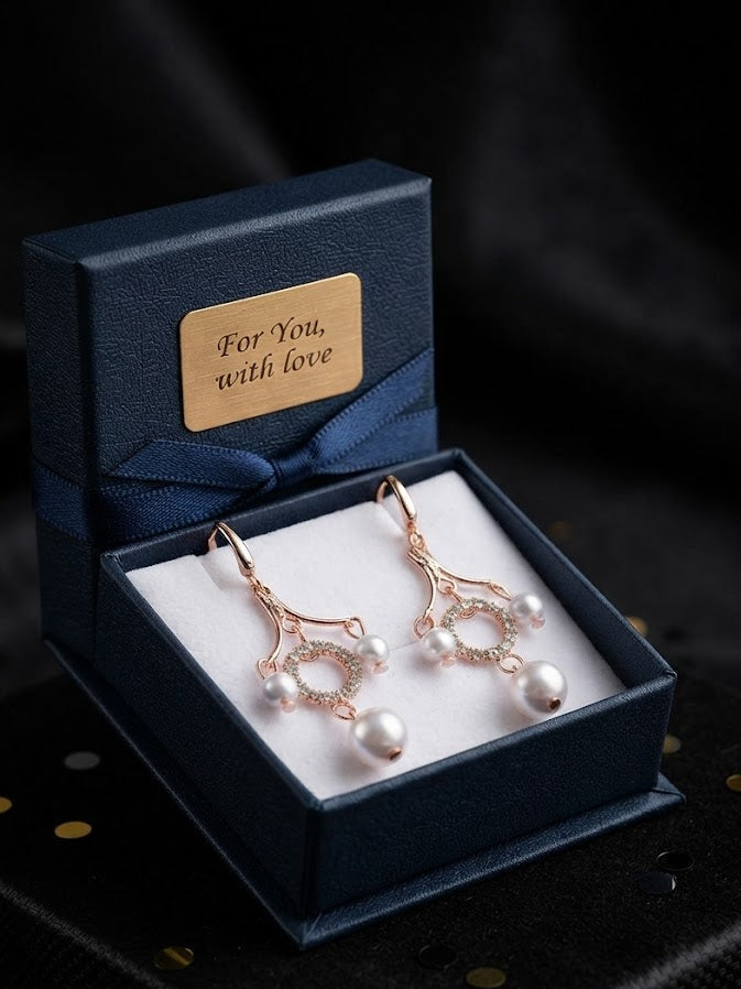 Rose gold CZ pavé circle pearl chandelier leverback drop earrings displayed on a T-bar stand inside an open luxury burl wood jewellery box with navy blue quilted velvet interior, gold brass fittings, perfume bottles and ballet shoes in the background – AureliaBlends