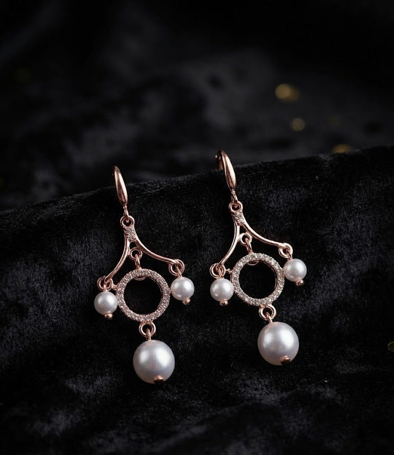 Rose gold CZ pavé circle pearl chandelier leverback drop earrings close-up on dark black velvet with scattered gold confetti dots showing leverback hook, fan frame arms, pavé CZ open circle halo and large pearl drop – AureliaBlends statement dangle earrings