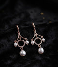 Rose gold CZ pavé circle pearl chandelier leverback drop earrings close-up on dark black velvet with scattered gold confetti dots showing leverback hook, fan frame arms, pavé CZ open circle halo and large pearl drop – AureliaBlends statement dangle earrings