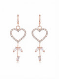 Model wearing rose gold pavé CZ open heart baguette crystal tassel leverback drop earrings with a sleek low chignon in a warm champagne luxury interior with a walnut jewellery box in the background – AureliaBlends bridal earrings side profile