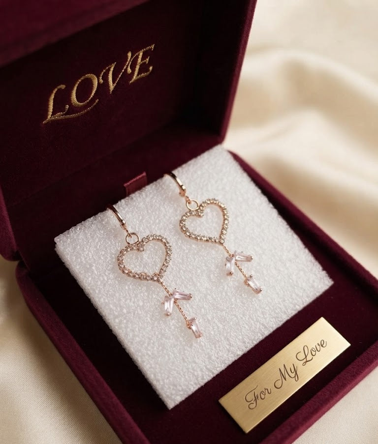 Rose gold pavé CZ open heart baguette crystal tassel leverback drop earrings on a dark black velvet and glass surface showing open heart pavé CZ frame, leverback hoop and three baguette crystal tassel drops – AureliaBlends dark editorial statement earrings