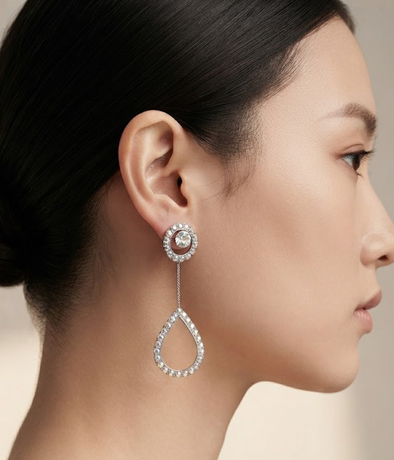 Silver CZ round halo solitaire chain teardrop pavé long drop earrings flat lay on white marble with scattered iridescent crystal bicone beads, a navy blue jewellery box and a silver fountain pen with a champagne silk scarf – AureliaBlends sparkle editorial