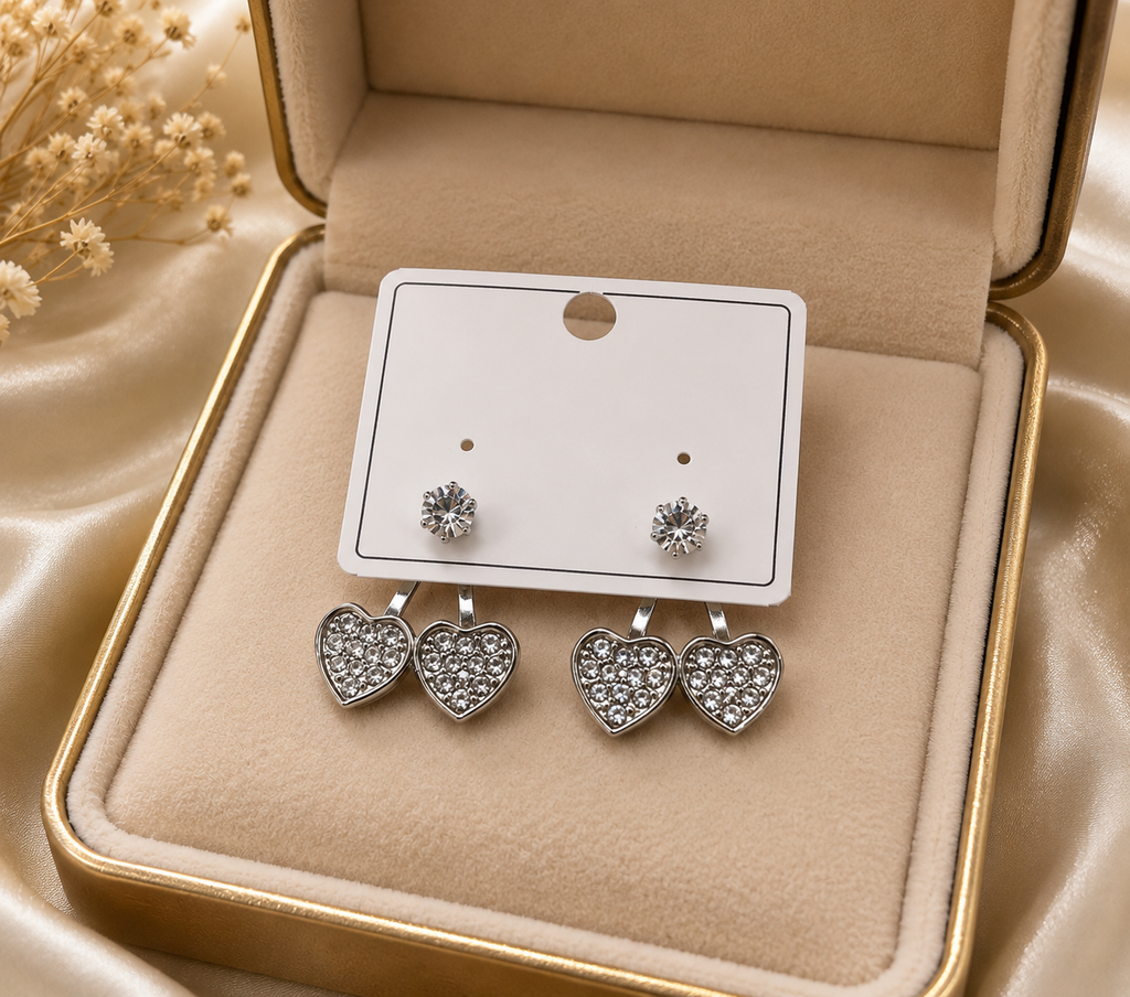 Silver CZ double heart ear jacket earrings flat lay on white marble with loose CZ stones, a cream leather jewellery case, gold pen and Diamond Heart Collection tag – AureliaBlends